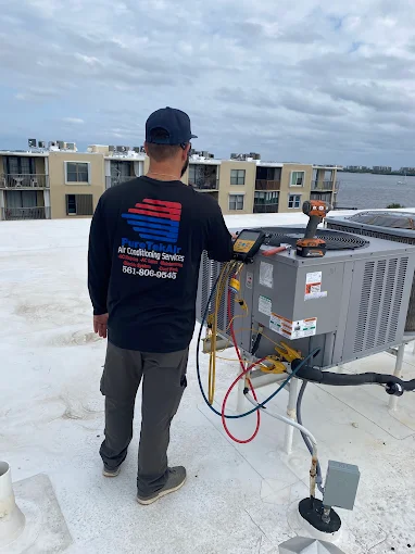 Technician in a Pure Tek Air shirt servicing an outdoor AC condenser on a rooftop with a digital manifold gauge